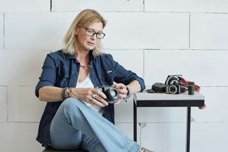 Modern mature lady photographer with blond hair checking camera before photo shoot in studioの写真素材