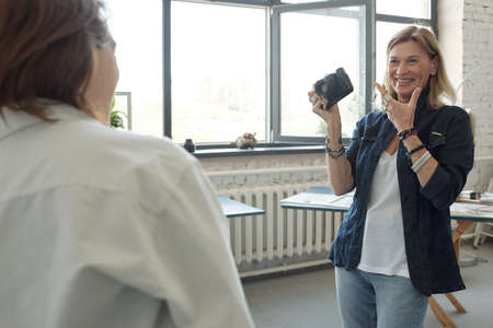 Cheerful mature photographer with camera asking model to smile in photo studioの写真素材