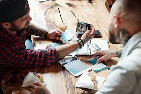 Over shoulder view of modern man showing travel photographs to friend while they gathering in cafe