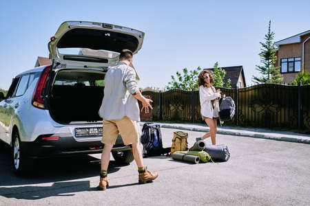 Happy young couple collecting bags with baggage into car trunk on sunny day