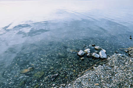Pebbles under pure transparent water of lake or river and part of bank consisting of stones of various shapes and sizesの写真素材