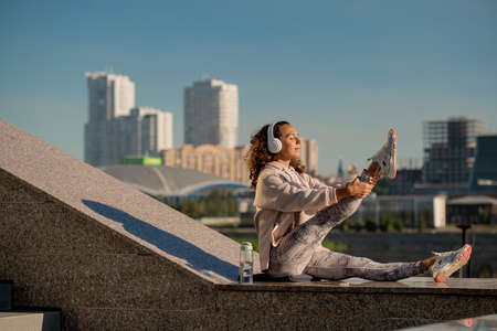 Young active female in sportswear listening to music or audio training in headphones while exercising on marble structure outdoorsの写真素材