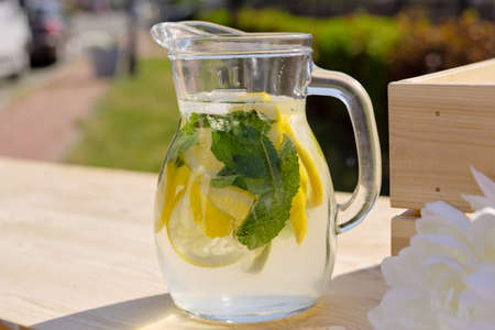 Glass jug with fresh cool homemade lemonade standing on wooden market stall on sunny day in natural...