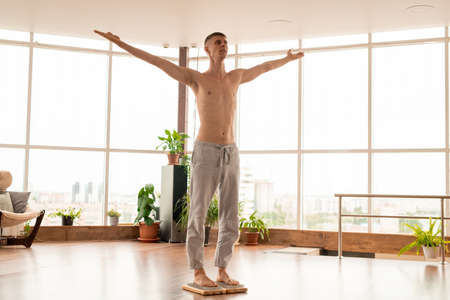 Young active shirtless man in sportspants keeping his arms outstretched while standing on yoga therapy pads with metallic bristlesの写真素材