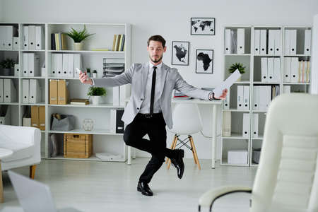 Concentrated fashionable young male lawyer holding contract and balancing on one leg to focus on thoughtsの写真素材