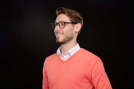 Smiling confident handsome young bearded guy in eyeglasses looking aside against black background, purpose conceptの写真素材
