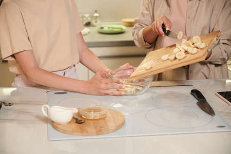 Young female putting banana slices into glass bowl during cooking masterclass