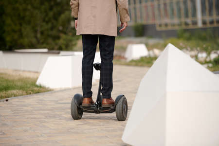 Back view of contemporary man in pants and trenchcoat standing on gyroscope