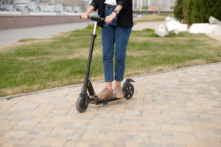 Legs and hands of young contemporary female standing on electric scooterの写真素材