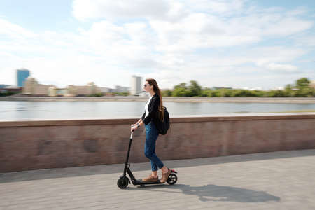 Young carefree female in casualwear and sunglasses moving on electric scooter