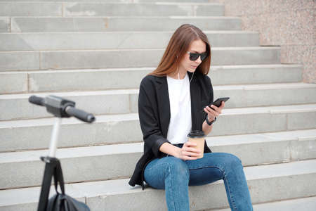 Young casual woman with smartphone sitting on staircase in urban environmentの写真素材