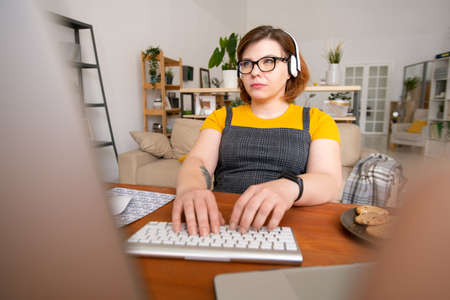 Young serious female with headphones looking at data on computer screen