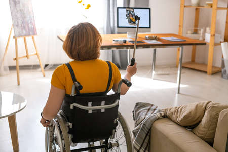 Back view of young contemporary female in wheelchair moving across her new houseの写真素材