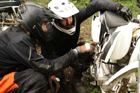 Concentrated motorcyclists in helmets examining belly pan of motorcycle while discussing reason of...