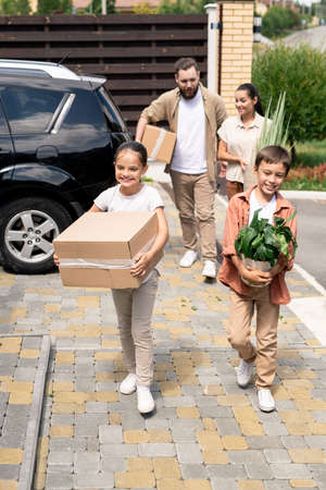 Cheerful cute children carrying moving stuff into new house together with parentsの写真素材