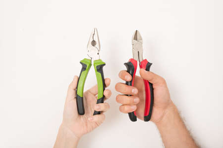 Close-up of unrecognizable people holding different pliers against white wall, renovation concept