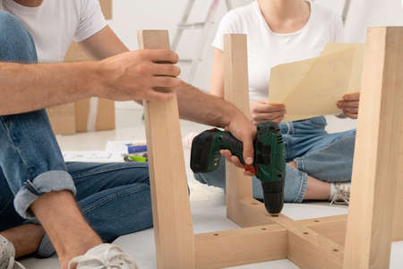 Close-up of unrecognizable man sitting on floor and using screwdriver while assembling table with wifeの写真素材