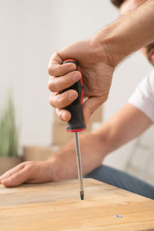 Close-up of man turning screw into wooden board while assembling furnitureの写真素材