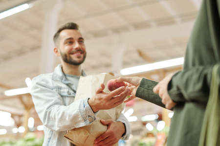 Below view of unrecognizable woman giving juicy peach to husband while they buying fruits at marketの写真素材