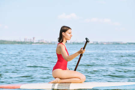 Young serene sportswoman in red swimsuit floating on water at summer resort