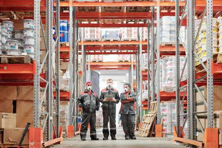 Group of intercultural warehouse workers in gloves, respirators and workwearの写真素材