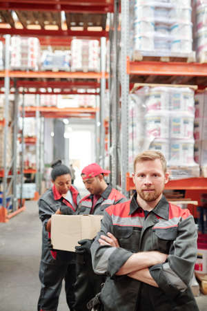 Bearded man in workwear standing in front of camera on background of colleaguesの写真素材