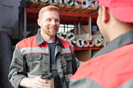Smiling worker in uniform having coffee during conversation with colleagueの写真素材