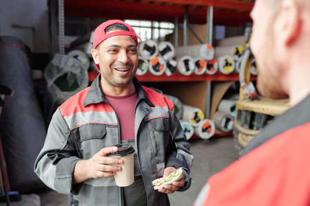 Happy mixed-race warehouse worker having coffee with sandwich for lunchの写真素材