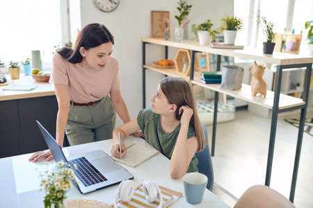 Young mother bending over desk where her teenage daughter studyingの写真素材