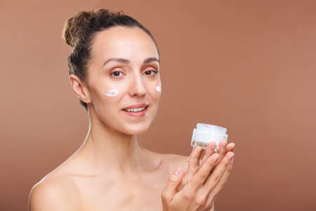 Young beautiful woman with healthy skin holding jar with moisturizing creamの写真素材