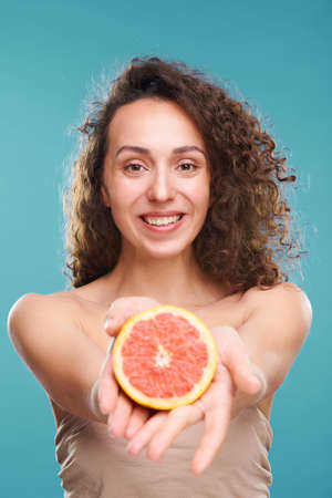 Beautiful young woman with healthy skin and toothy smile holding grapefruitの写真素材