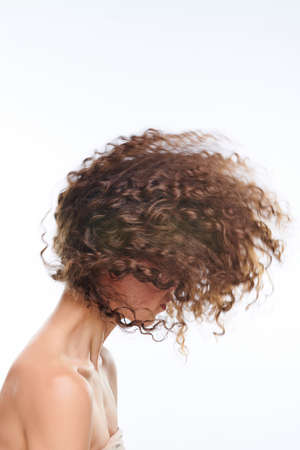 Side view of young fresh gorgeous woman with dark long wavy hair hiding her faceの写真素材