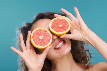 Young cheerful woman holding slices of fresh juicy grapefruit by her eyesの写真素材