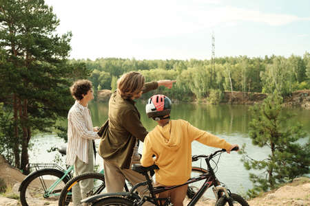 Young man pointing at opposite riverbank while talking to his son and wife