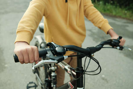 Hand of contemporary teenage boy pushing bicycle while moving down roadの写真素材