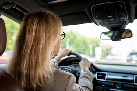 Woman with blond hair looking through front window while driving for meetingの写真素材