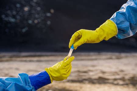Gloved hand of ecologist in coveralls taking flask with sample of polluted waterの写真素材