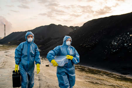 Two female ecologists in coveralls, respirators, eyeglasses and rubber gloves