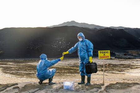 Contemporary ecologist in protective workwear taking sample of polluted water