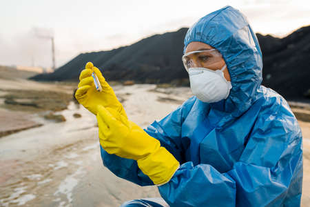 Young female ecologist or researcher looking at flask with sample of soil