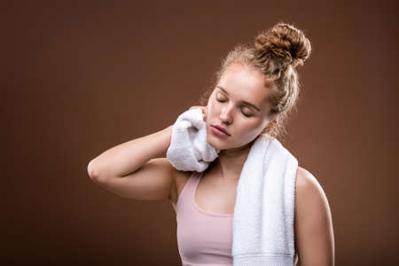 Tired fit girl in sportswear rubbing her neck with white soft towel at breakの写真素材