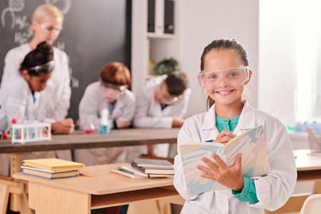 Happy cute pupil of secondary school in whitecoat and eyeglasses looking at youの写真素材