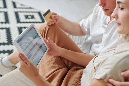 Young affectionate couple sitting on sofa and buying airplane tickets online