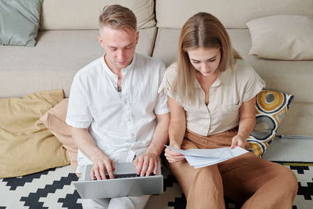 Young married business partners entering data and reading pages of contract