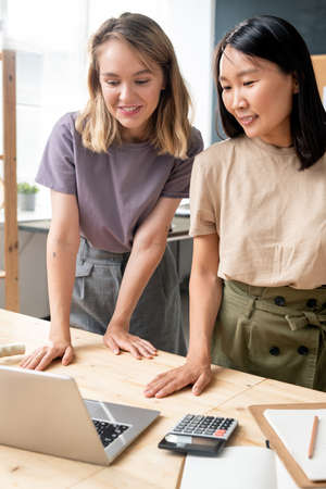Two happy young businesswomen in casualwear looking at laptop displayの写真素材