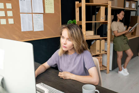 Two contemporary young female workers of storage room taking online orders
