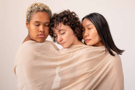 Group of young intercultural females with closed eyes wrapped into white linen