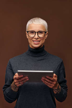 Young smiling blond businesswoman in smart casualwear holding touchpad