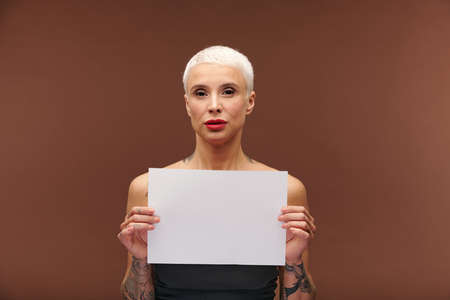 Contemporary young blond businesswoman with tattoos on arms holding blank paperの写真素材
