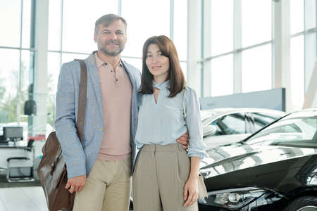Cheerful affectionate middle aged couple inside large contemporary auto center